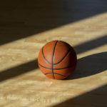 Basketball on hardwood court floor with natural lighting.