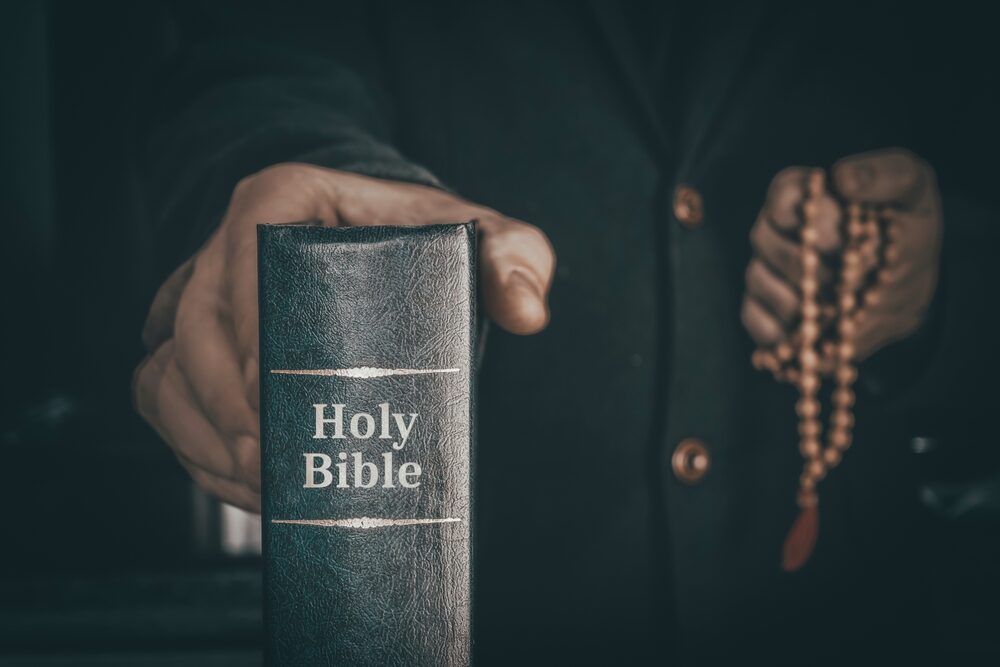 priest holding a bible and rosary beads