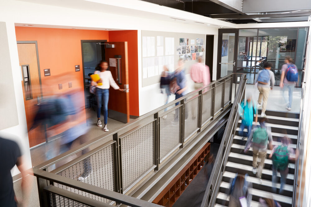 blurred image of a busy high school corridor with students walking upstairs and in hall