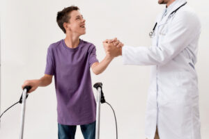 male doctor shaking hands with cheerful disabled boy with cerebral palsy, taking steps using his walker