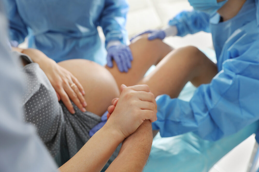 closeup of a Woman giving birth in maternity hospital with support of doctors and spouse