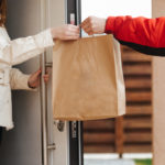 The food delivery man passes the craft package to the customer at the door of her house