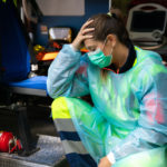 Portrait of a young woman doctor sitting on the ambulance resting exhausted where a first aid intervention during the Covid-19 pandemic