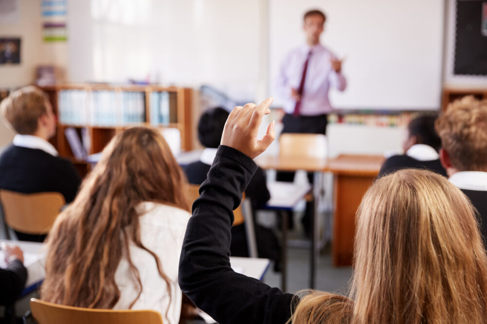 Female Student Raising Hand To Ask Question In Classroom