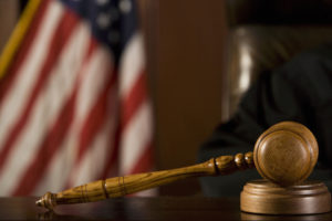 Close up of a judge's gavel with American flag in the background of courtroom