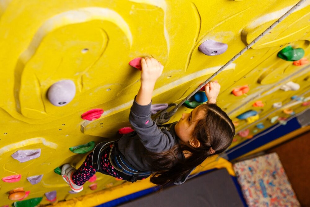 little girl climbing a rock wall indoor.