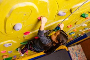 little girl climbing a rock wall indoor.