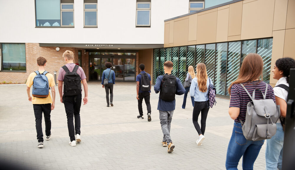 Rear View Of High School Students Walking Into building