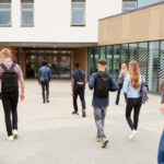 Rear View Of High School Students Walking Into building