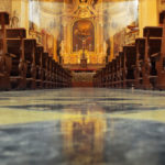 Interior of a beautiful old catholic church from below with marble floor, wooden pews, and light streaming onto altar with Jesus on crucifix