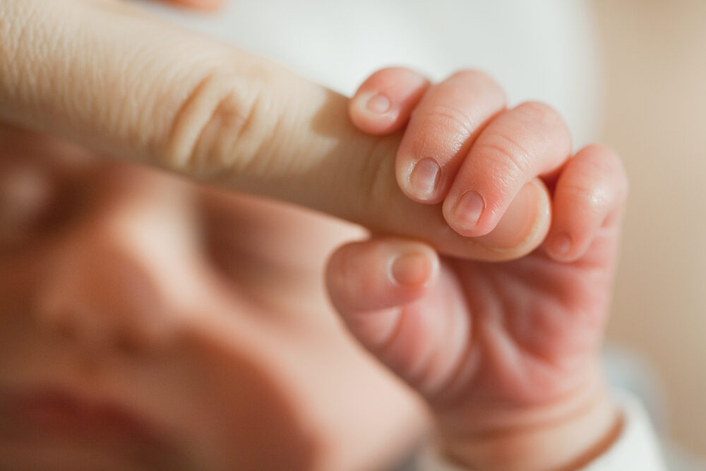 a newborn baby holding on to mother's finger closeup