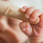 a newborn baby holding on to mother's finger closeup