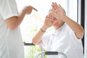 An elderly woman holds her hands up to protect herself from a worker