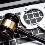 A gavel and handcuffs on a laptop keyboard