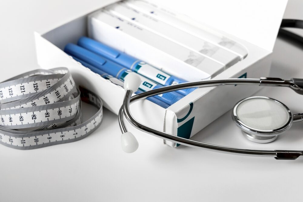 box of ozempic injector pens and refills on a white table with a stethoscope and tape measure laying beside