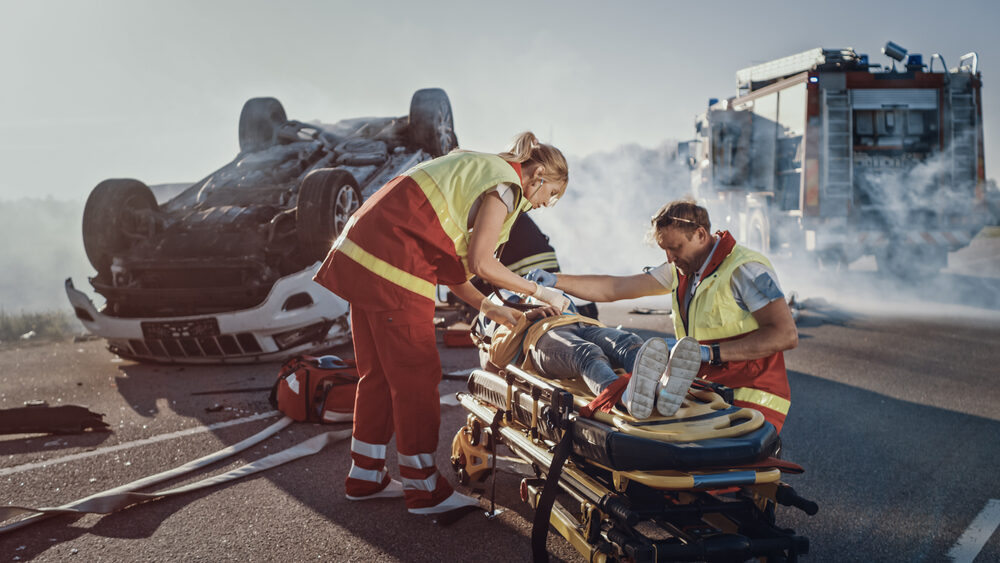 paramedics assisting a young woman on a stretcher at an overturned vehicle accident scene