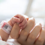 a premature baby holds on to mother's finger closeup