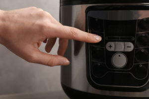 woman's hand pressing pressure cooker button to begin cooking.