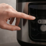 woman's hand pressing pressure cooker button to begin cooking.