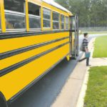 Students hop off a yellow school bus at a school bus stop