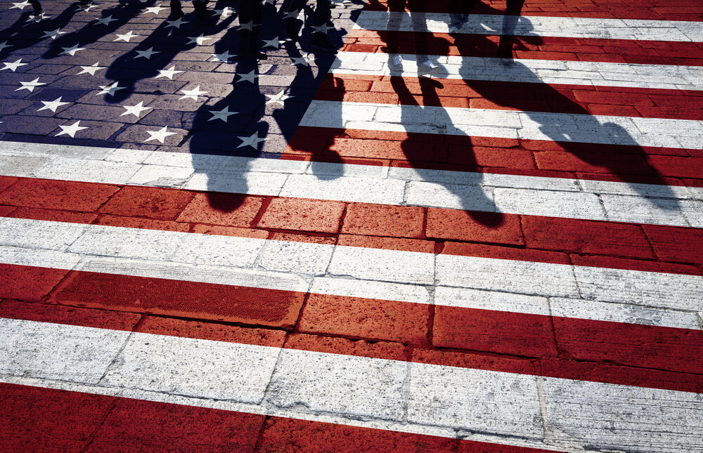 shadows of people walking on a roadway painted like the us flag