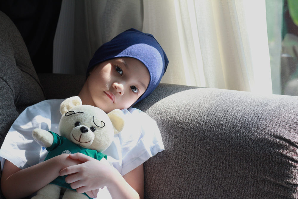 A young girl wearing a headscarf clutches a teddy bear