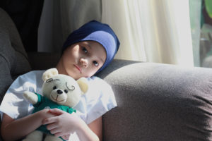 A young girl wearing a headscarf clutches a teddy bear