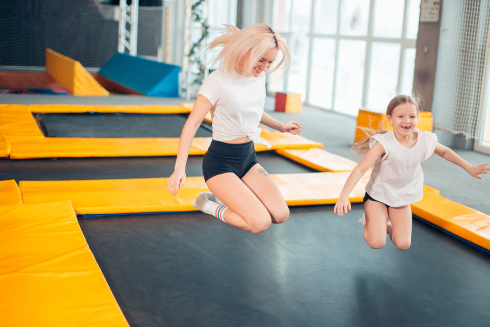 An older and younger sister bounce on a trampoline indoors