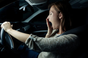 A woman yawns as she drives her car at night