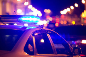 Flashing blue lights atop a police car, with blurred city lights in the background