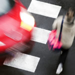 A red car about to strike a pedestrian at a crosswalk, as seen from above