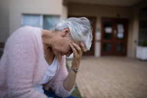 An elderly woman alone in a hallway with her head in her hands