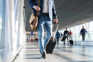 A man pulls his wheeled luggage through an airport terminal