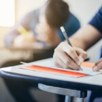 male high school student at desk taking a test with pencil in hand