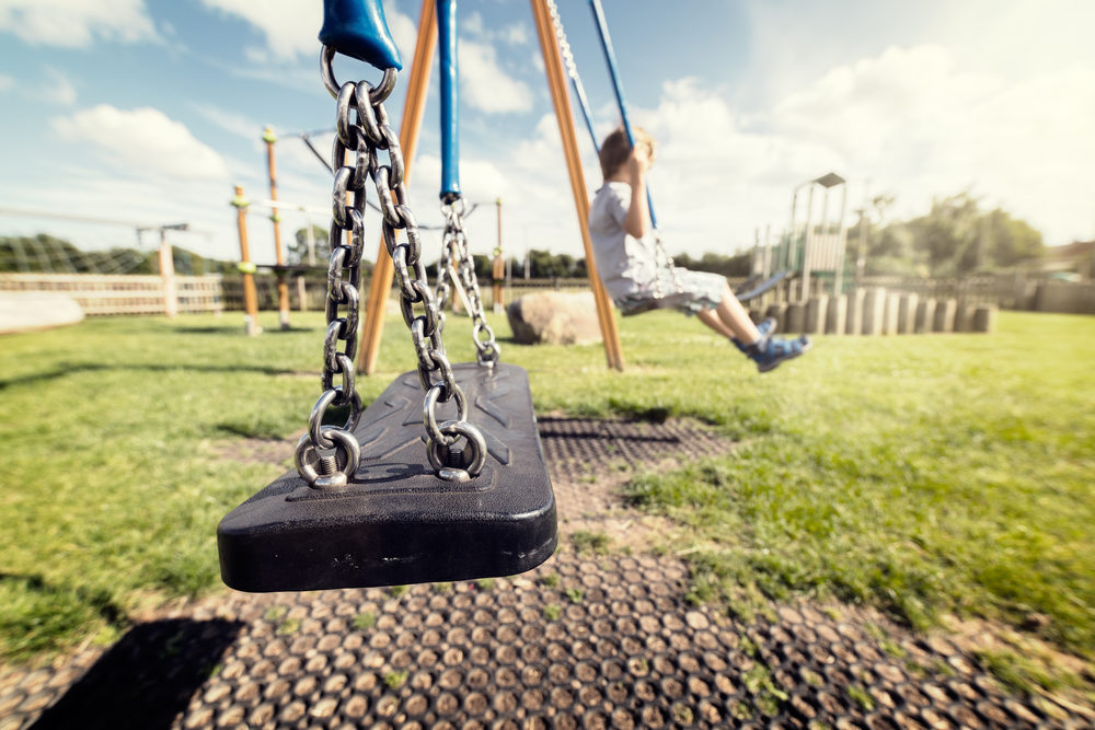 Empty playground swing with a child on the next swing