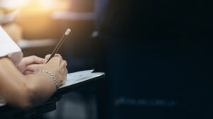 .high school student at desk with hand holding pencil writing on test paper answer sheet