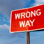 A red "Wrong Way" road sign against a cloudy sky