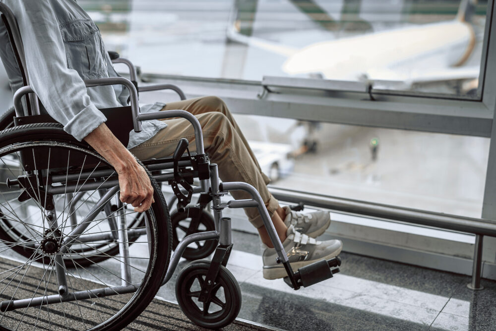 Cropped photo of mature lady on wheelchair waiting in airport hall with airplane in the background