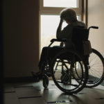 lonely senior woman looking through the window of the nursing home.