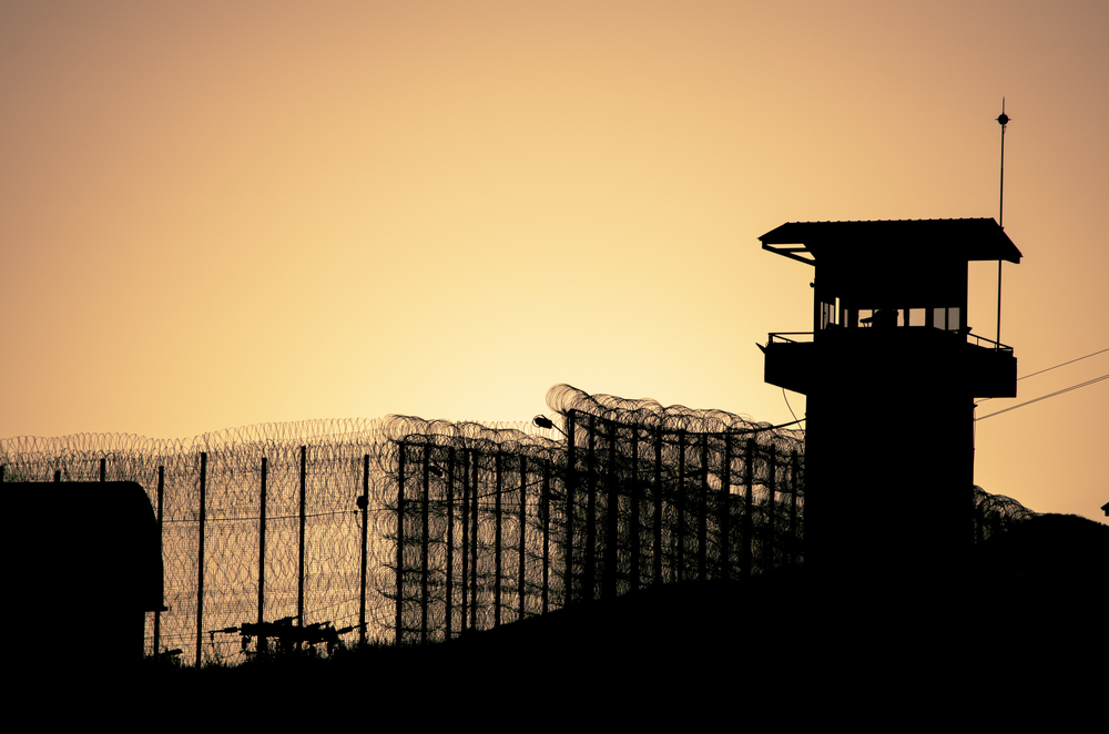 Silhouette of barbed wires and watchtower of prison, at sunset