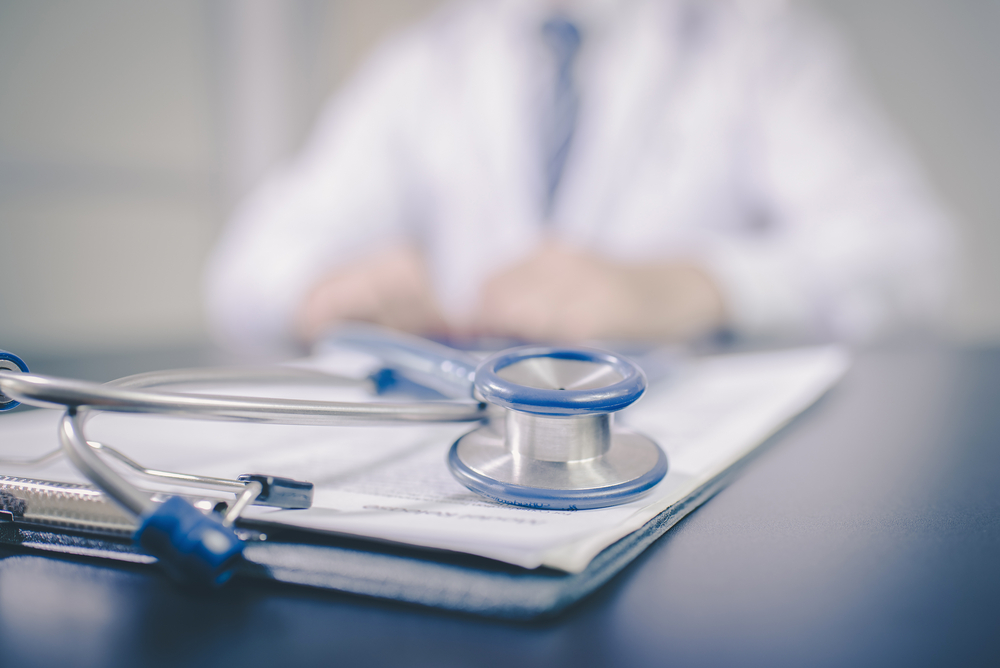 stethoscope on notepad at desk with blurred doctor in background