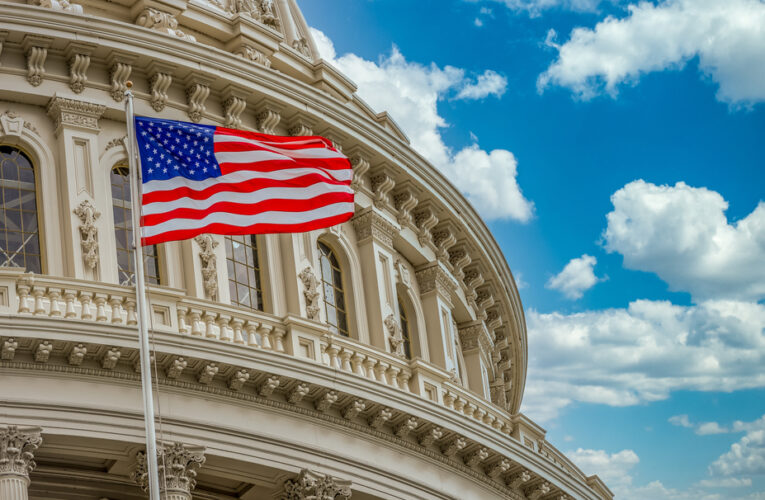 American flag flies in front of the US capitol building in Washington DC with blue cloudy sky background