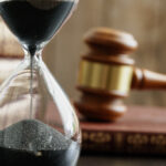 closeup of an hourglass with blurred focus on a gavel and law books in background