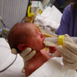 Premature newborn being fed formula from a nurse in hospital