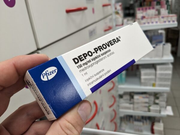 closeup of a hand holding a box of depo-provera birth control medication in a pharmacy